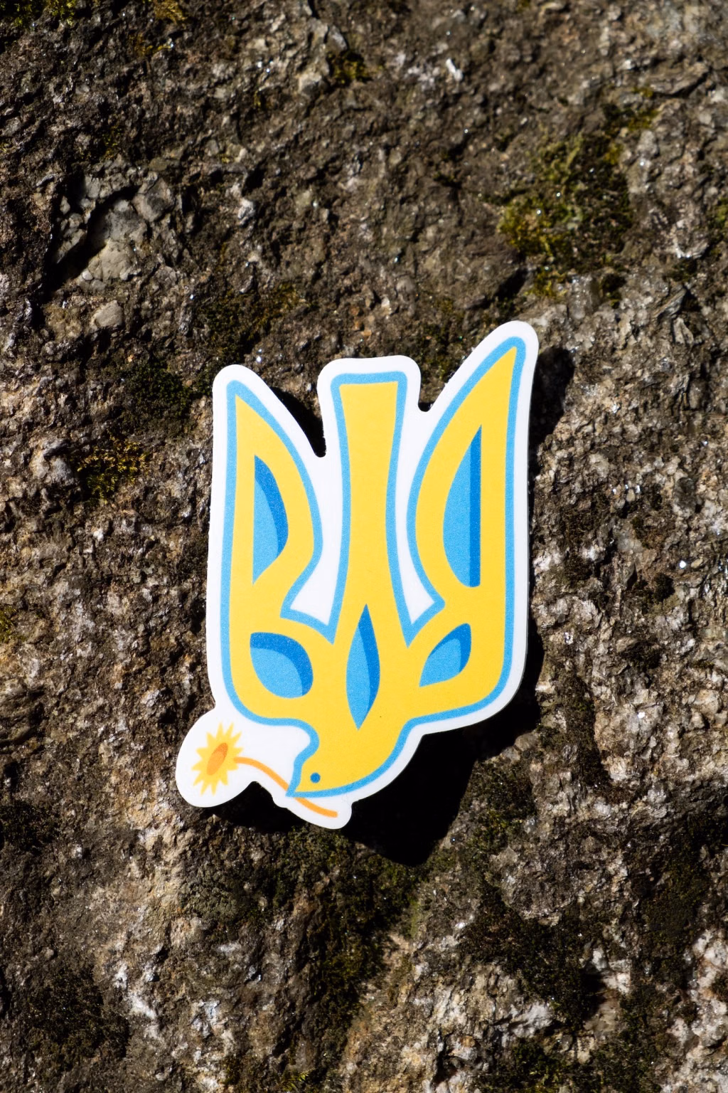 Photo of the Ukrainian trident dove sticker placed on a mossy grey rock