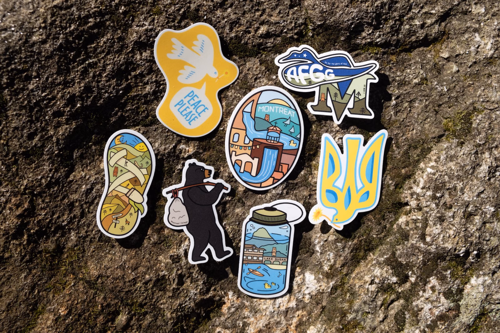 Photo of all seven finished Montreat stickers arranged together on a mossy grey rock